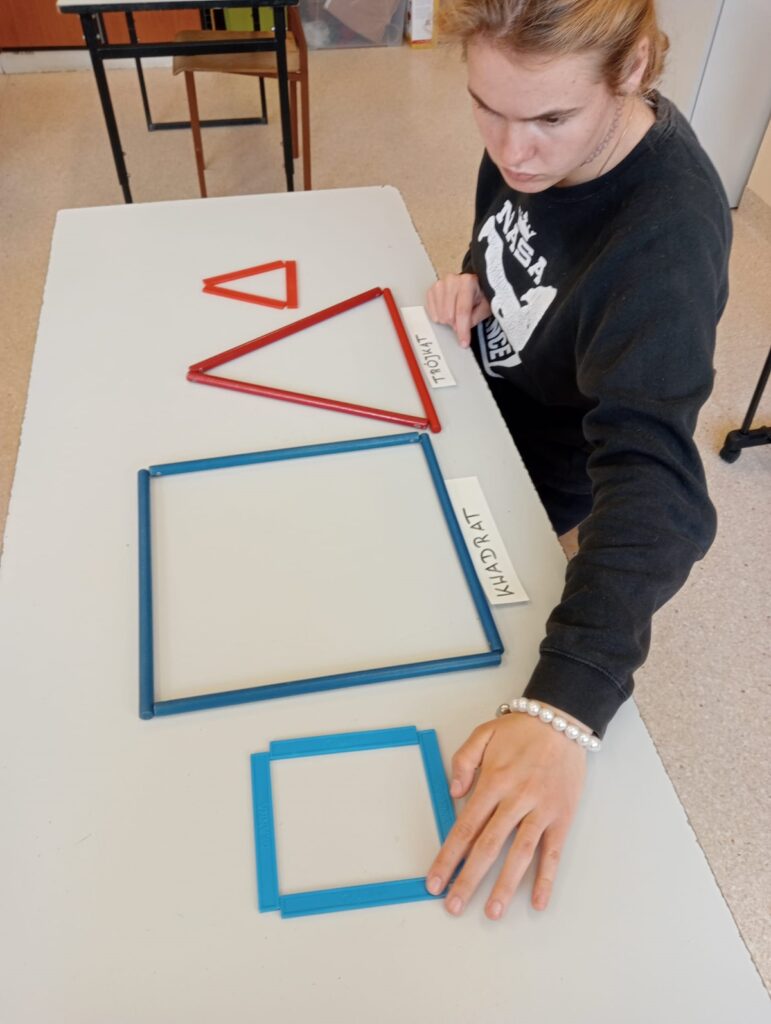 Uczennica układa na ławce kształty figur geometrycznych - kwadrat i trójkąt