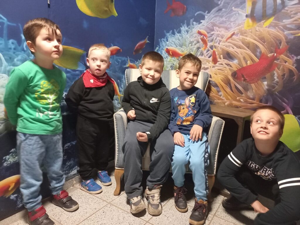 Oceanarium.  Piątka chłopców stoi na tle ściany z wizualizacją wodnego świata i uśmiecha się.